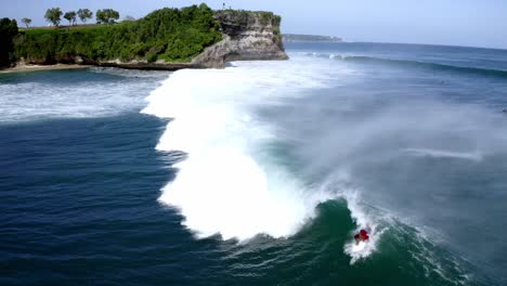 Männlicher-Surfer-Im-Roten-Hemd-Fängt-Eine-Große-Vier-Meter-Lange-Welle-Am-Strand-Von-Balangan,-Während-Sie-Kracht,-Kamerafahrt-Mit-Dem-Dolly-Aus-Der-Luft