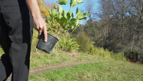 Toma-En-Cámara-Lenta-De-Un-Hombre-De-Negocios-Que-Lleva-Una-Planta-Y-Una-Pala-A-Través-De-Un-Campo