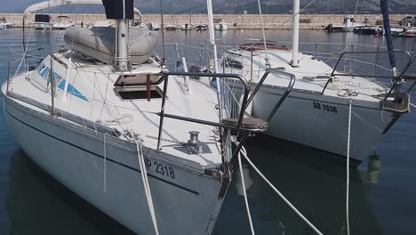 Two-white-sailboats-bob-gently,-moored-in-a-sunny-Mediterranean-marina