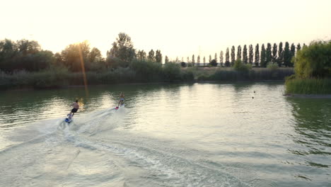 A-young-couple-flying-across-a-clam-recreational-lake,-racing-each-other,-aerial-follow