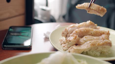 Person-Watching-Videos-On-Smartphone-While-Eating-A-Chicken-Fillet-On-Rice