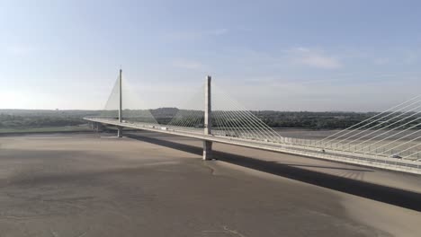 Vehicles-crossing-contemporary-Mersey-Gateway-bridge-aerial-view-at-low-tide-wide-pull-back