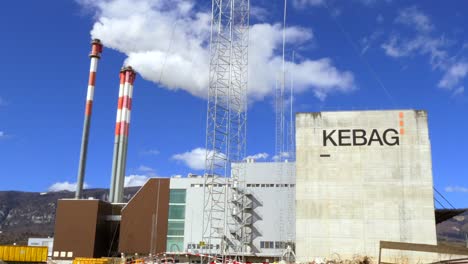 Zoom-out-shot-of-Incineration-plant-factory-Kebag-With-Smoking-Smokestack-in-Zuchwil,Switzerland