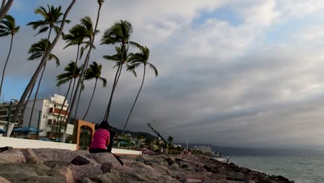 Eine-Person,-Die-Bei-Sonnenuntergang-Am-Meer-In-Puerto-Vallarta,-Mexiko,-Auf-Felsen-Sitzt