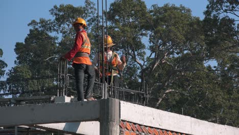 Amplia-Toma-Exterior-De-Trabajadores-De-La-Construcción-En-El-Techo-De-Un-Edificio-Con-Cascos-Y-Chaquetas-De-Alta-Visibilidad