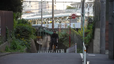 Asiatischer-Mann-Mit-Gesichtsmaske,-Der-Während-Einer-Pandemie-In-Der-Straße-Von-Tokio,-Japan,-Bergauf-Radelt