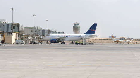 Tripulaciones-De-Tierra-Del-Aeropuerto-Que-Manejan-Un-Avión-De-Air-Cairo-En-La-Puerta-De-La-Terminal-De-Un-Aeropuerto-En-Alejandría,-Egipto---Plano-General