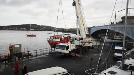 Camión-Grúa-Hidráulica-Que-Levanta-Un-Barco-De-Pesca-Pesado-En-El-Puerto-De-Gales-Conwy