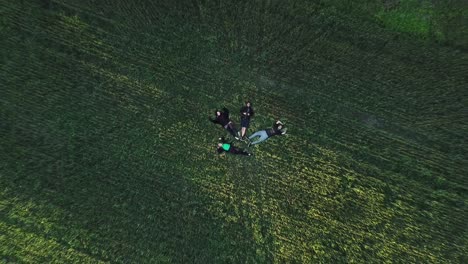 Grupo-De-Amigos-Tirados-En-El-Suelo-De-Hierba-Cerca-Del-Molino-De-Viento---Disparo-De-Drones-De-Arriba-Hacia-Abajo