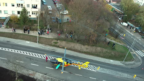 helicopter-rescue,-air-ambulance-standing-on-the-center-of-road-in-city,-a-crowd-of-onlookers-standing-around