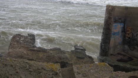 Big-waves-hitting-the-abandoned-concrete-coast-defense-building-ruins-with-graffiti-in-stormy-weather