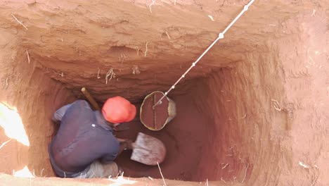 Un-Hombre-Africano-Dentro-De-Un-Agujero-Profundo-Que-Se-Está-Excavando-En-Una-Letrina-De-Pozo-Cargando-Tierra-En-Un-Balde-Para-Ser-Transportado