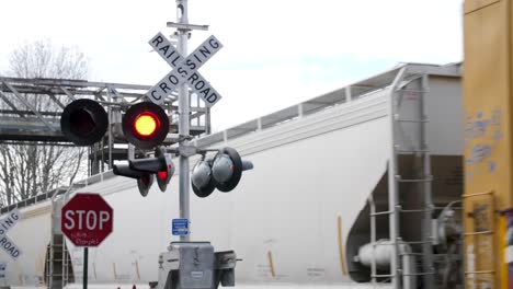 Aktives-Bahnübergangsschild-Mit-Vorbeifahrendem-Zug-Im-Hintergrund