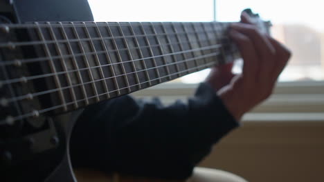 Man-Practising-a-vintage-black-electric-guitar,-rehearsing-chords,-solos-and-octaves-in-a-natural-light-environment.