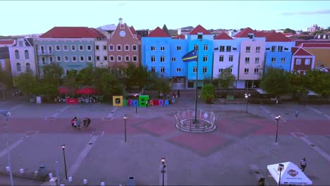 Revealing-aerial-shot-of-Otrobanda-district-in-Willemstad,-Curacao,-with-flag-on-pole,-colorful-buildings-and-the-Queen-Emma-bridge