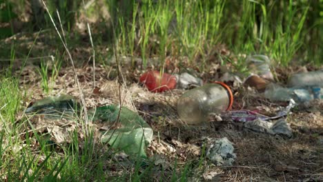 Basura-En-La-Naturaleza---Vertedero-Ilegal-Lleno-De-Basura-De-Plástico-Y-Vidrio,-Hierba-Y-árboles-En-El-Fondo,-Primer-Plano