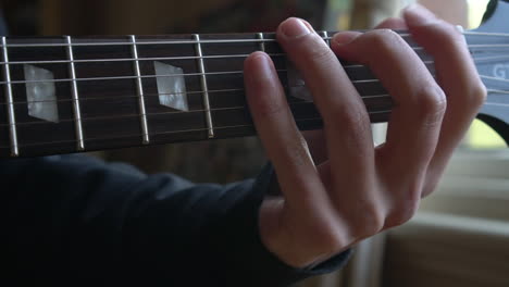 Man-Practising-a-vintage-black-electric-guitar,-rehearsing-chords,-solos-and-octaves-in-a-natural-light-environment.