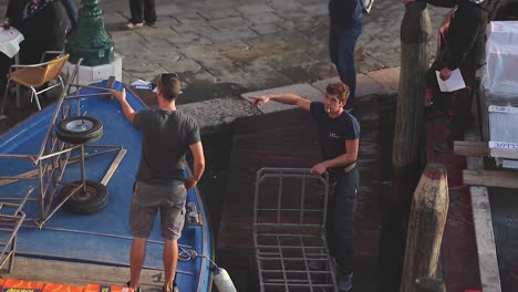 Workers-offload-merchants-from-blue-small-boat-in-a-Canal-Port-in-Slow-Motion-in-Venezia-City