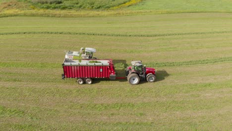 4K-Luftaufnahme-Mit-Schwenk-Nach-Rechts-Von-Einem-Mähdrescher,-Der-Heu-In-Einen-Traktor-Und-Einen-Wagen-Erntet