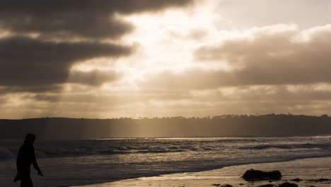 Las-Olas-Rompen-En-Cámara-Lenta-En-Coronado,-California,-Playa-Al-Atardecer-Mientras-La-Persona-Camina-A-Través-Del-Marco