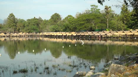 Beautiful-Huay-Tung-Tao-Lake-in-Chiang-Mai-with-a-lush-mountain-backdrop,-displaying-the-straw-huts-on-the-lake-front