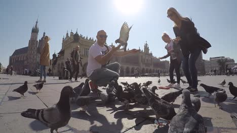 Familia-De-Turistas-Alimentándose-E-Interactuando-Con-Palomas-En-La-Plaza-De-Cracovia