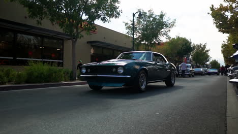 Pristine-classic-blue-Chevy-Camaro-cruises-past-downtown,-tracking