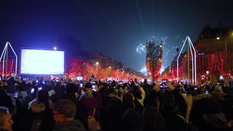 Grandes-Fuegos-Artificiales-Y-Celebraciones-Durante-La-Llegada-Del-Nuevo-Año-En-Los-Principales-Campos-Elíseos-De-París,-Rodeados-Por-Una-Multitud-De-Personas-En-La-Calle-Principal-Con-Vistas-Al-Arco-Triunfal-Y-La-Calle-Cubierta-De-Rojo