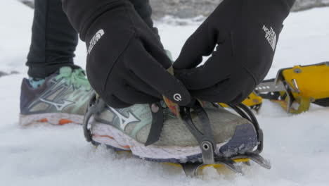 Cerca-De-Manos-Enguantadas-Atándose-Crampones,-Preparándose-Para-Una-Caminata-Por-El-Glaciar,-Cámara-Lenta