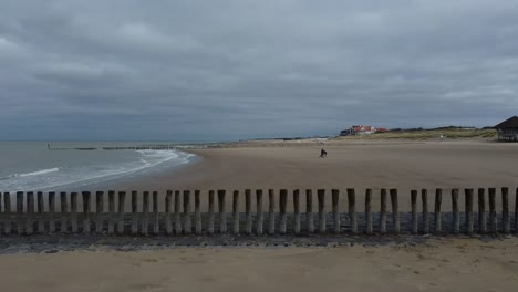 Volando-Con-Un-Dron-De-Lado-Pasando-Una-Fila-De-Postes-De-Madera-Hacia-El-Mar-En-Holanda