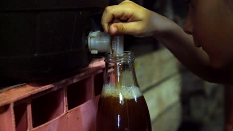 Apple-cider-juice-served-at-a-mill-on-bottle-by-young-boy-instructed-by-father,-Close-up-handheld-shot