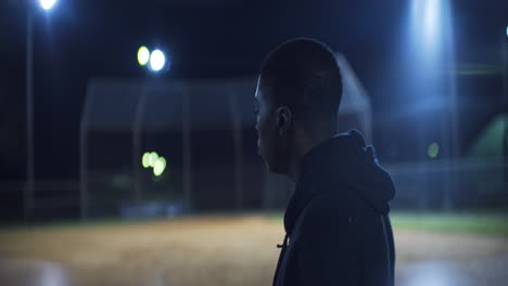 African-American-Teen-Walks-on-Baseball-Field-at-Night,-Profile-Medium