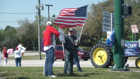 Donald-Trump-Anhänger-Stehen-An-Einer-Straßenecke-Mit-Schildern-Und-Fahnen,-Die-An-Einem-Sonnigen-Tag-In-Südflorida-Ihre-Unterstützung-Für-Donald-Trump-Zeigen