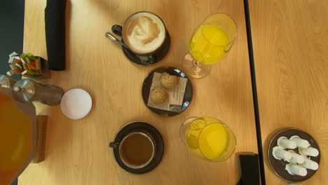 breakfast-on-table,-coffee,-cappuccino,-mugs,-orange-juice,-cups-and-bakery