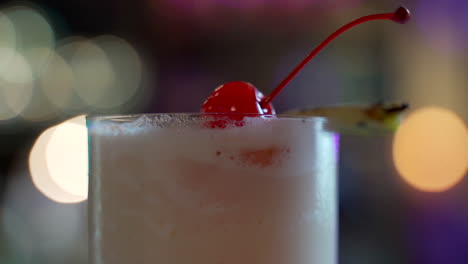 piña-colada-detail-shot-of-top-garnish-cherry-pineapple-spinning-in-bar-lights