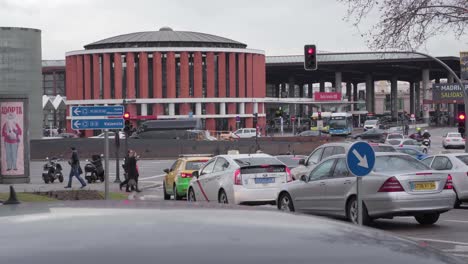 Verkehrsszene-Auf-Der-Straße-Tagsüber-In-Madrid,-Spanien-Mit-Dem-Bahnhof-Madrid-Atocha-Im-Hintergrund-–-Totalaufnahme