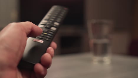 Presionando-El-Botón-De-Netflix-En-El-Control-Remoto-De-La-Televisión,-El-Primer-Plano-De-La-Mano-Masculina,-La-Pantalla-Borrosa-En-El-Fondo