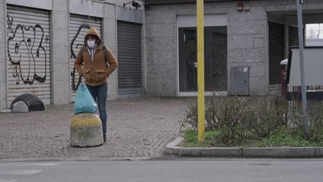 Un-Hombre-Con-Máscara-Y-Chaqueta-Con-Capucha-Esperando-Para-Cruzar-La-Calle-En-Arcore,-Italia,-Plano-General