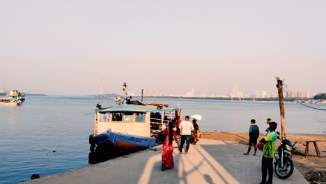 Eine-Kleine-Fähre,-Die-Am-Steg-Geparkt-Oder-Angedockt-Ist,-Und-Ein-Tourist,-Der-In-Die-Fähre-Einsteigt,-Mit-Wunderschönem-Mumbai-Stadthintergrund-In-Der-Nähe-Einer-Bucht-In-Mumbai