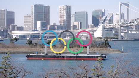 Monumento-De-Los-Anillos-Olímpicos-En-Odaiba-Con-El-Puente-Del-Arco-Iris-Y-El-Horizonte-De-Tokio-En-El-Fondo-En-Japón