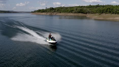 Man-races-along-a-large,-tropical-lake-on-a-jet-ski---aerial-view