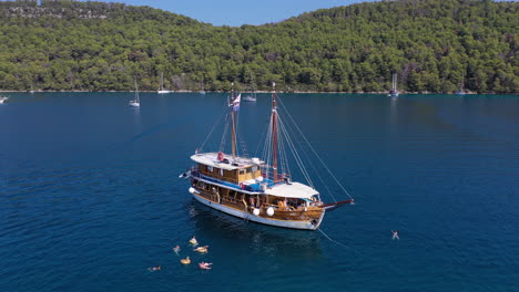 People-swimming-in-sea-beside-yacht-on-travel-holiday,-aerial-arc-shot