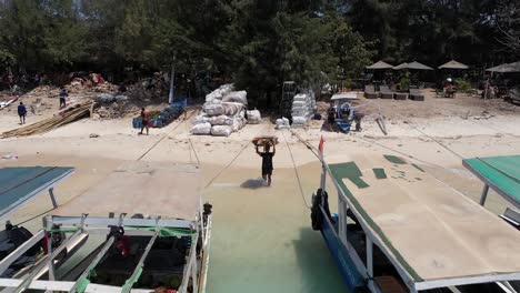 Paquete-De-Cajas-De-Cartón-En-La-Cabeza-Del-Hombre-Para-Cargar-En-Un-Barco---Reciclaje-De-Materiales-De-Basura-En-La-Isla-De-Gili-Trawangan,-Indonesia---Retirada-De-Drones