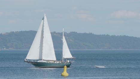 Un-Velero-Verde-De-Dos-Mástiles-Tira-De-Un-Lúgubre-A-Través-De-La-Bahía-De-Comienzo,-Puget-Sound,-Y-Pasa-Una-Boya-Amarilla