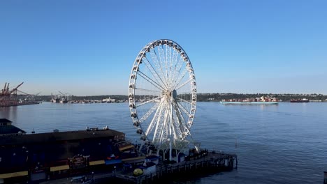 Rising-up-revealing-the-Great-Wheel-of-Seattle-and-sunrise-illuminating-Elliot-Bay,-aerial