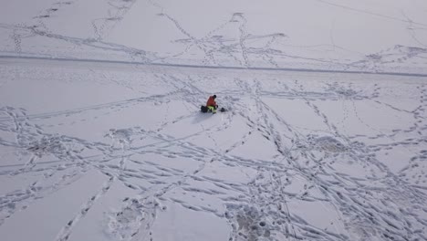 Slight-overhead-zoom-in-on-lonesome-outdoor-guy-fishing-through-small-hole-on-a-big-frozen-lake