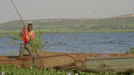 Nahaufnahme-Eines-Afrikanischen-Fischers,-Der-Mit-Einer-Großen-Stange-Sein-Traditionelles-Holzkanu-Am-Ufer-Des-Victoriasees-Zu-Wasser-Lässt