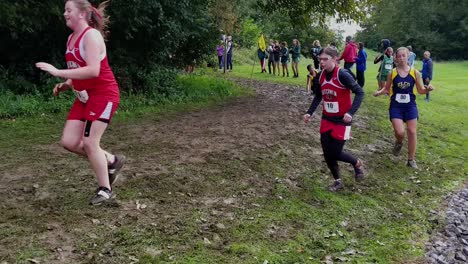 Mehrere-Cross-Country-Läuferinnen-Rutschen-Aus-Und-Fallen-In-Einer-Kurve,-Laufwettbewerb-Der-Mittelstufe,-Nasser-Und-Rutschiger-Langlaufpfad-Im-Wald