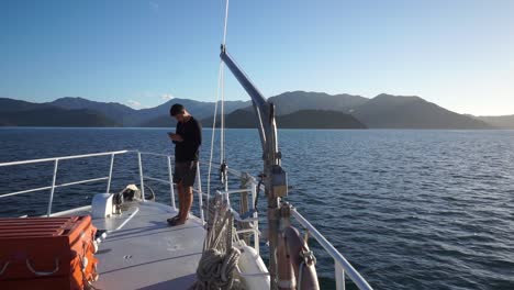 Young-male-standing-on-front-deck-of-cruise-boat-with-beautiful-scenery-in-background-during-evening