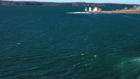 Er-Neigt-Sich-Von-Einer-Welle,-Die-In-Einem-Blaugrünen-Ozean-Aufsteigt,-Nach-Oben-Und-Zeigt-In-Der-Ferne-Einen-Leuchtturm